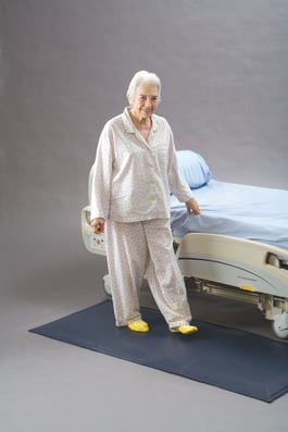 Woman standing on floor cushion sensor next to a hospital bed